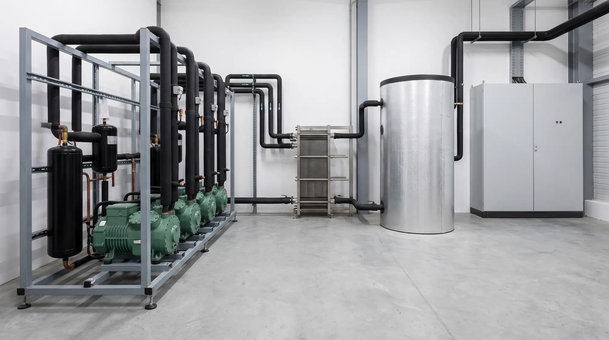 Salle des machines avec une centrale frigorifique à quatre compresseurs, un échangeur à plaques et un ballon tampon calorifugé