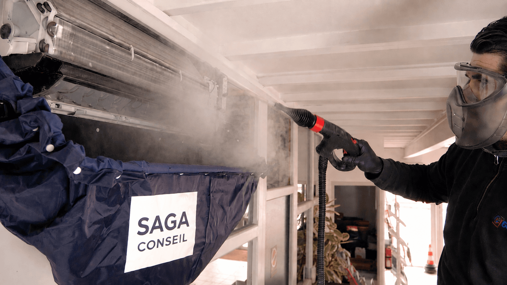 Technicien SAGA CONSEIL nettoyant une unité intérieure de pompe à chaleur air/air avec une bâche de protection