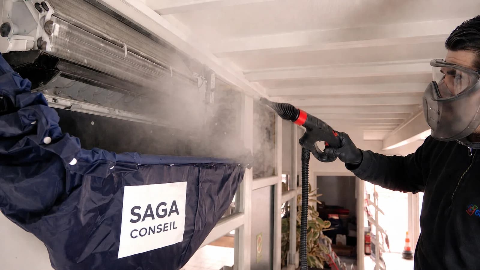 Technicien SAGA CONSEIL nettoyant une unité intérieure de pompe à chaleur air/air avec une bâche de protection